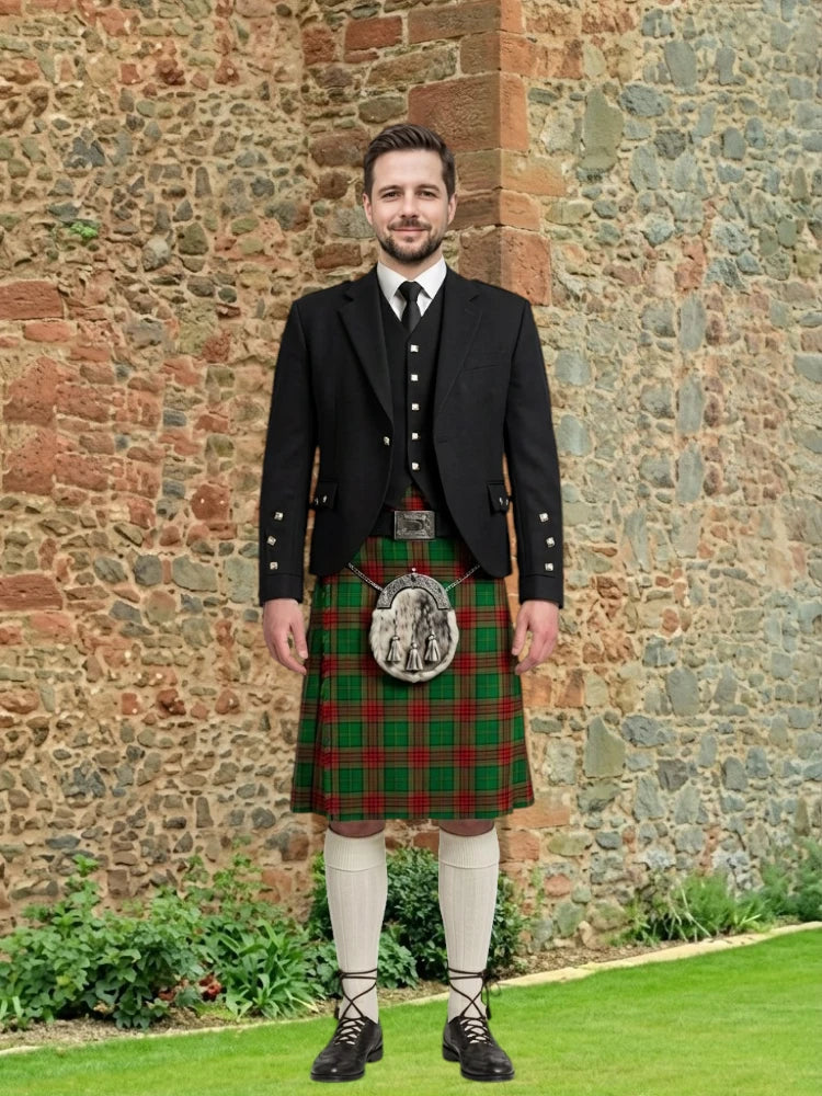 Man wearing a traditional Scottish kilt standing in front of a stone wall.