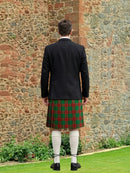 Person wearing a black jacket and red plaid kilt standing in front of a stone wall.