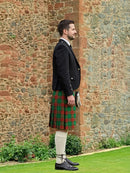 Man wearing a traditional Scottish kilt standing against a stone wall.