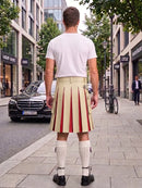 A man standing on a city sidewalk, viewed from behind, wearing a white t-shirt and a pleated kilt with vertical red and beige stripes, paired with white knee-high socks and black shoes.