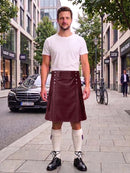 A man stands on a city sidewalk wearing a black leather kilt, white t-shirt, white knee-high socks, and black leather shoes. A black Mercedes-Benz car is parked on the street behind him, with buildings, trees, and a bicycle in the background.