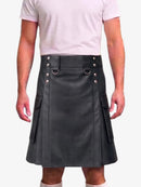 A man wearing a black faux-leather kilt with silver-tone metal hardware, a matching belt, and side cargo pockets, paired with a light pink t-shirt against a plain white background.