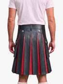 A man wearing a black pleated leather kilt with red vertical stripe accents and silver-tone metal buttons, paired with a light pink t-shirt, shown from the back against a light gray background.