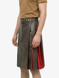 Person wearing a green leather skirt with red accents and studded details on a white background