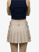 Person wearing a navy tank top and beige pleated skirt on a white background