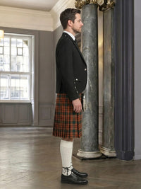 Man wearing a black jacket and red plaid kilt in an elegant interior setting.