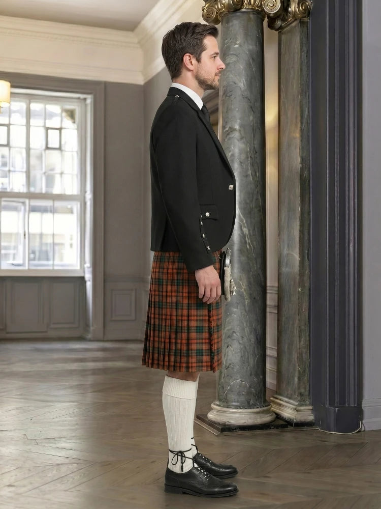 Man wearing a black jacket and red plaid kilt in an elegant interior setting.