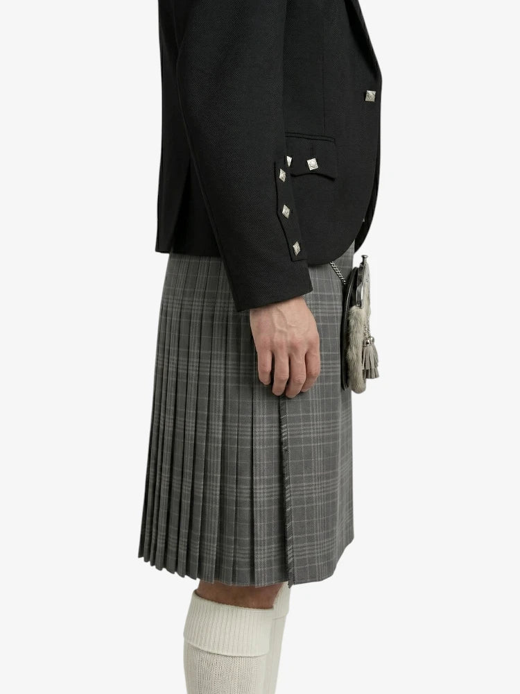 Person wearing a black blazer and gray pleated kilt on a white background