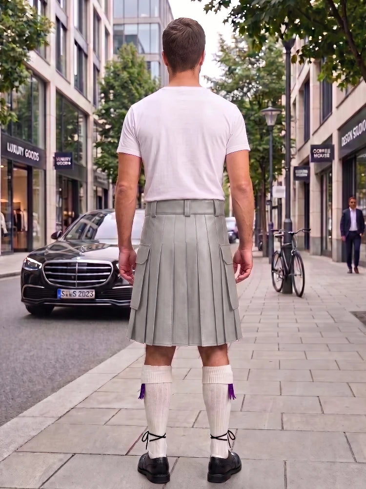 A man viewed from behind wearing a white t-shirt and a pleated light gray kilt, standing on a city sidewalk with a Mercedes-Benz car and storefronts in the background.