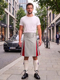 A man stands on a city sidewalk wearing a white t-shirt, a light gray kilt with red side panels, white knee-high socks, and black shoes. Buildings, trees, a parked black car, and a bicycle are visible in the background.
