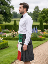 A man standing in a formal garden wearing a white dress shirt, black bow tie, and a kilt with an Irish flag pattern and a black leather strap system.