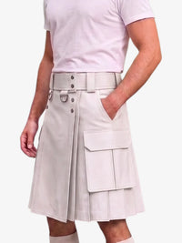 A model wearing a light beige kilt with a matching belt, silver hardware, and large cargo pockets, paired with a light pink t-shirt against a plain white background.